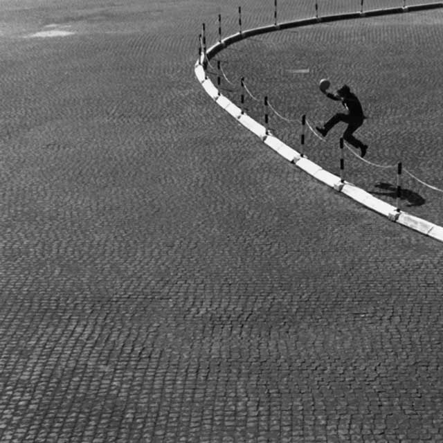 piazza con un bambino che salta staccionata con pallone in mano