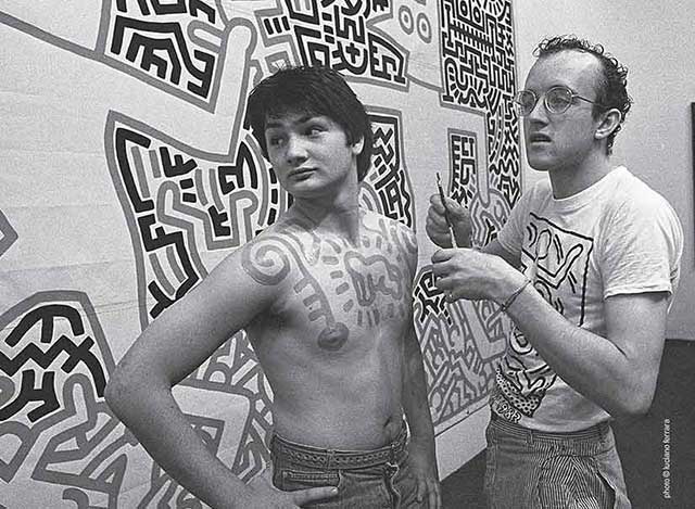 keith haring disegna dei graffiti con il pennello sul petto di un ragazzo