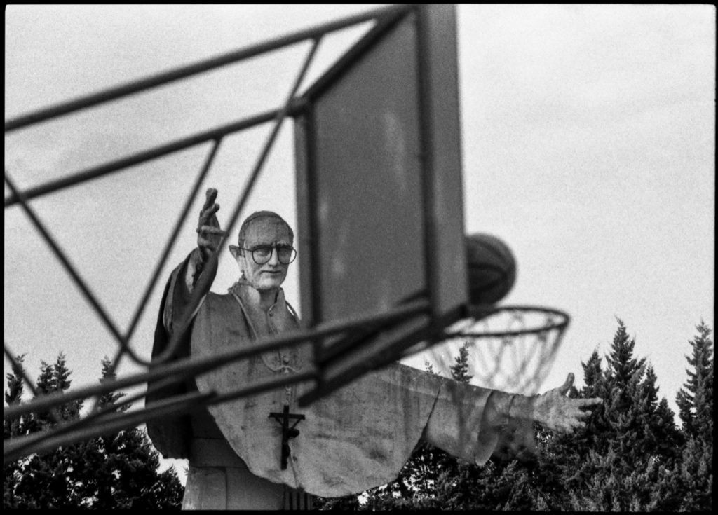fotografia in bianco e nero di statua di papa dietro a canestro di basket