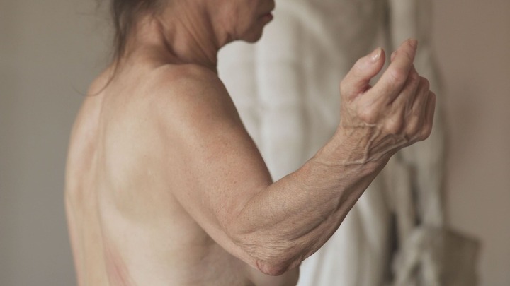 fotografia a colori di busto di donna anziana nuda con un braccio alzato