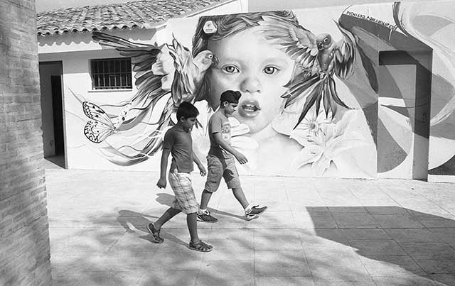 fotografia in bianco e nero di ragazzi che camminano per strada con dietro murales di volto di bambina