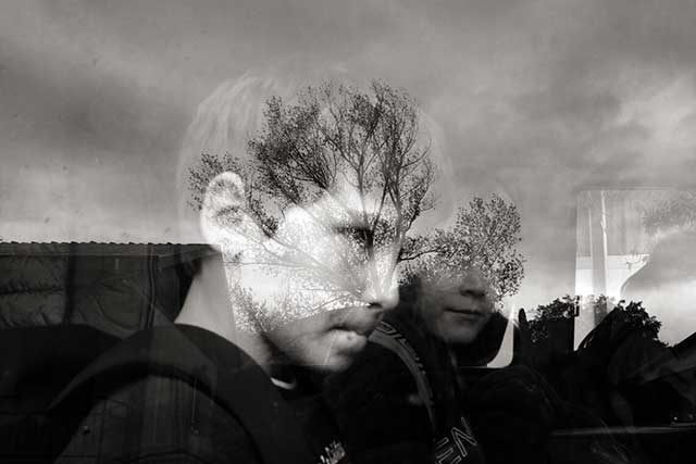 bambini dietro un vetro con riflessi degli alberi sul viso