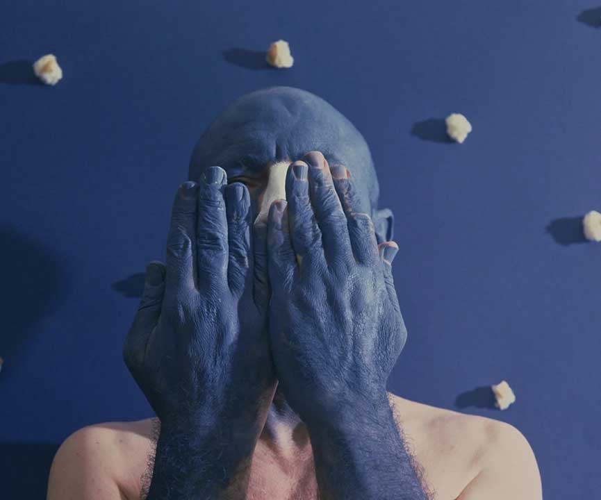 uomo pelato che si copre la faccia con la testa e le mani dipinte di blu