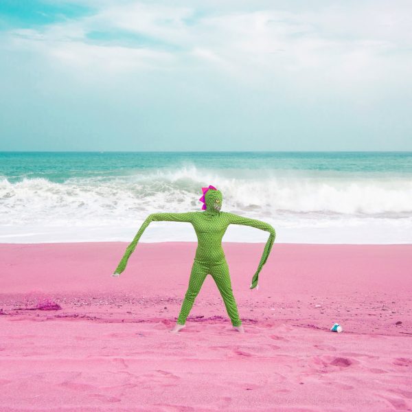 donna con costume verde con le maniche lunghe e cresta rosa su una spiaggia rosa con dietro il mare mosso
