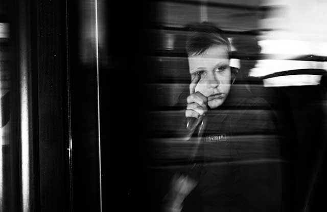 bambino con espressione triste mano sul viso e dito sull'occhio che guarda lontano da una finestra