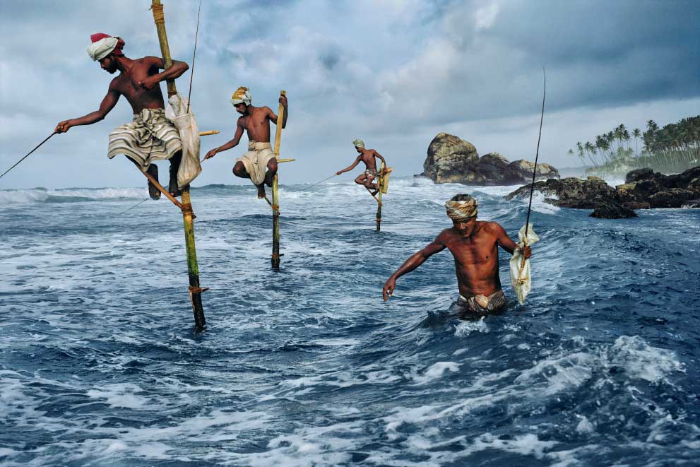 pescatori arrampicati su bastoni di legno in mezzo al mare