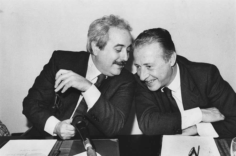 i giudici Falcone e Borsellino seduti vicino che si parlano sorridenti