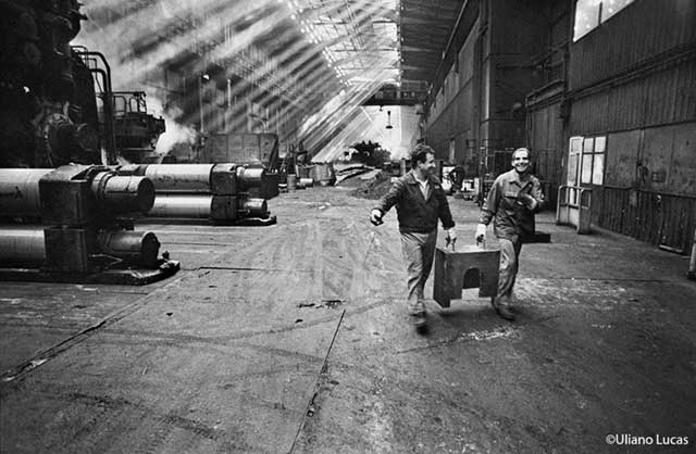 uomini sorridenti in una fabbrica che trasportano una cassaa