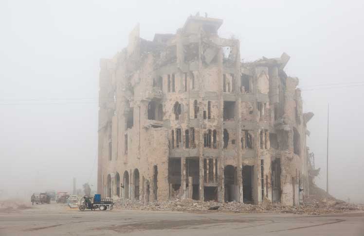 Enorme palazzo nella nebbia quasi completamente distruttoe sulla strada alcuni uomini che trascinano dei carretti