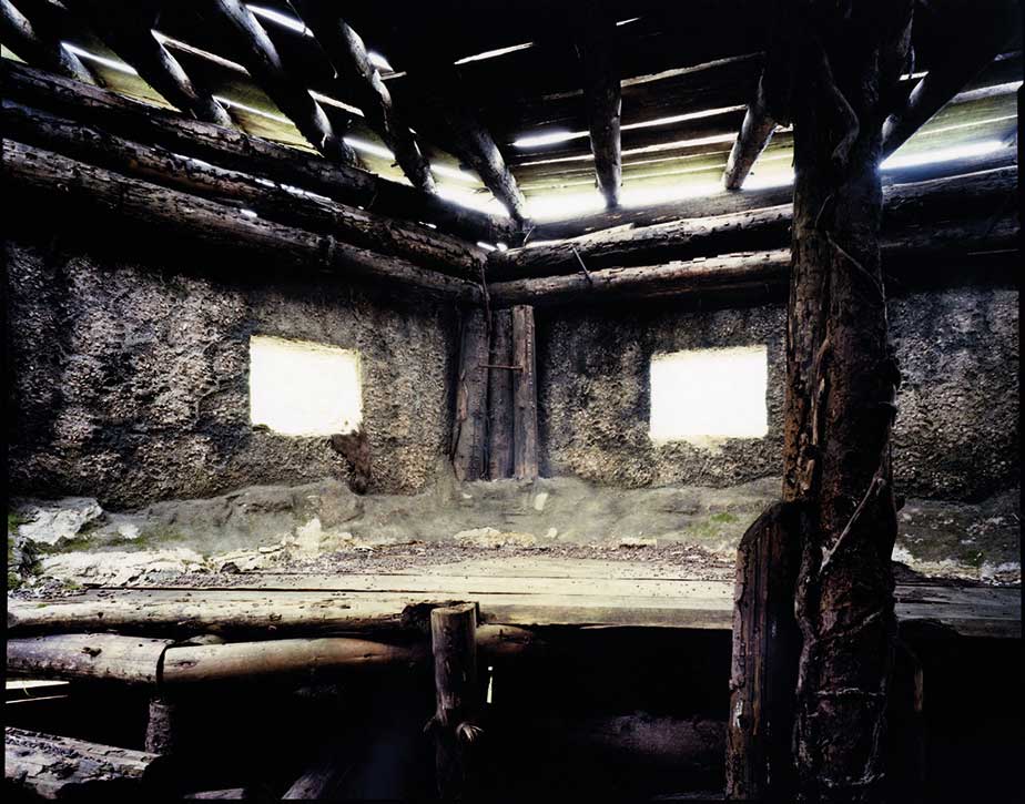 interno di casa con tetto e pavimento di legno e infondo due finestre illuminate da luce esterna