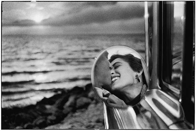 dettaglio di specchietto della macchina parcheggiata davanti al mare con riflessi uomo e donna sorridente che si baciano