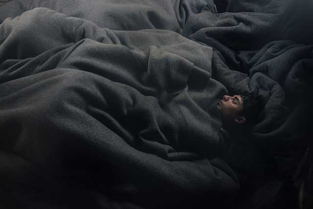 ragazzo che dorme circondato da coperte grigie