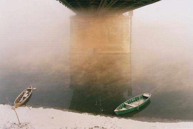 Giovanni Chiaramonte realismo infinito. due barche sulla riva di un fiume sotto un ponte