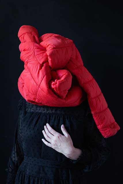 donna con vestito nero mano sul seno e piumone arancione che le avvolge la testa