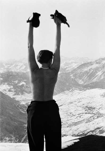 donna di spalle con collana di perle a torso nudo con le braccia alzate davanti a montagne innevate