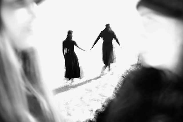 immagine sfocata di uomo e donna di spalle con cappotto lungo che camminano tenendosi la mano