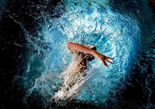 nuotatore che fa una bracciata alzando spruzzi visto dall'alto circondato da cerchio di luce azzurra