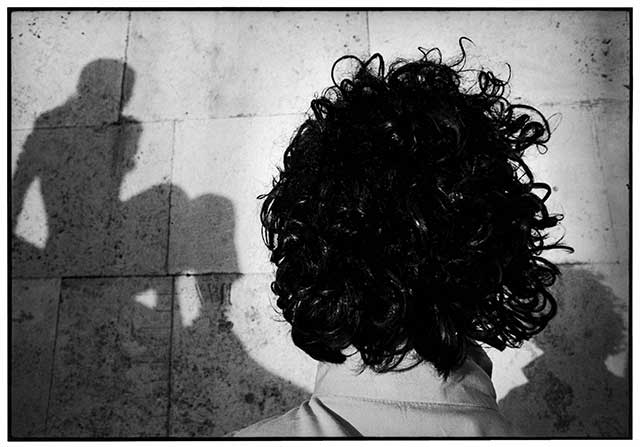 Pino Pascali e Ugo Mulas, Dialoghi dettaglio della testa di spalle di artista Pino Pascali che guarda un muro di mattoni con di lato un ombra di uomo seduto