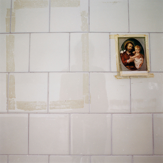 fotografia di muro di mattonelle bianche con alone di immagine staccata e santino attaccato con lo scotch
