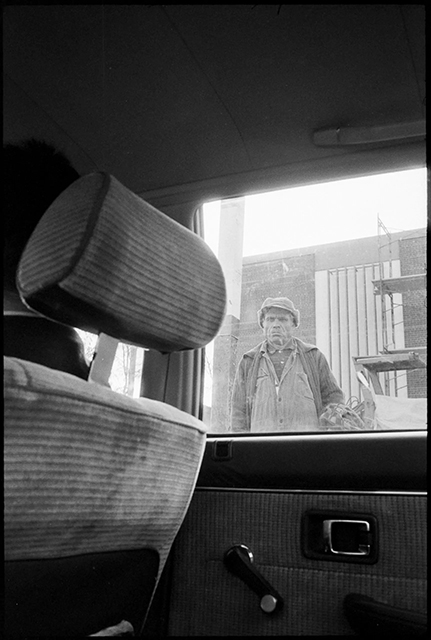 SALVATORE PIERMARINI E VITO TETI foto in bianco e nero di uomo per la strada con sguardo serio cappello e giacca visto dal finestrino di una macchina