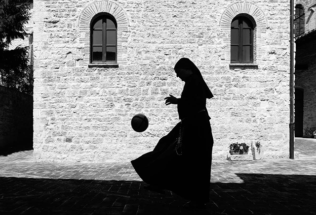 stefano guindani foto in bianco e nero silhouette si suora di profilo che gioca con la palla nel cortile di palazzo con muri di mattoncini e piccole finestre con le persiane chiuse