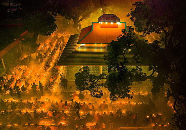 Vicino/lontano foto a colori scattata di notte dall'alto di abitazione indiana illuminata circondata da quattro file di persone sedute in terra in mezzo a tane luci