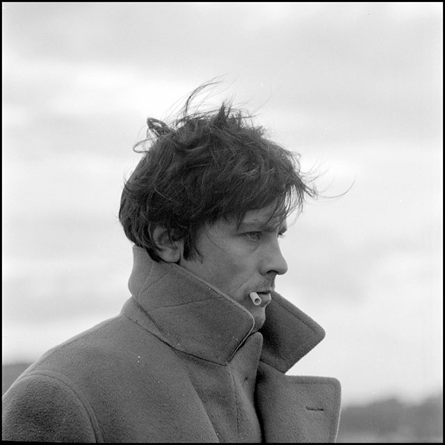 la prima notte di quiete foto in bianco e nero di primo piano l'attore Alain Delon di profilo con sigaretta in bocca e cappotto con il bavero rialzato