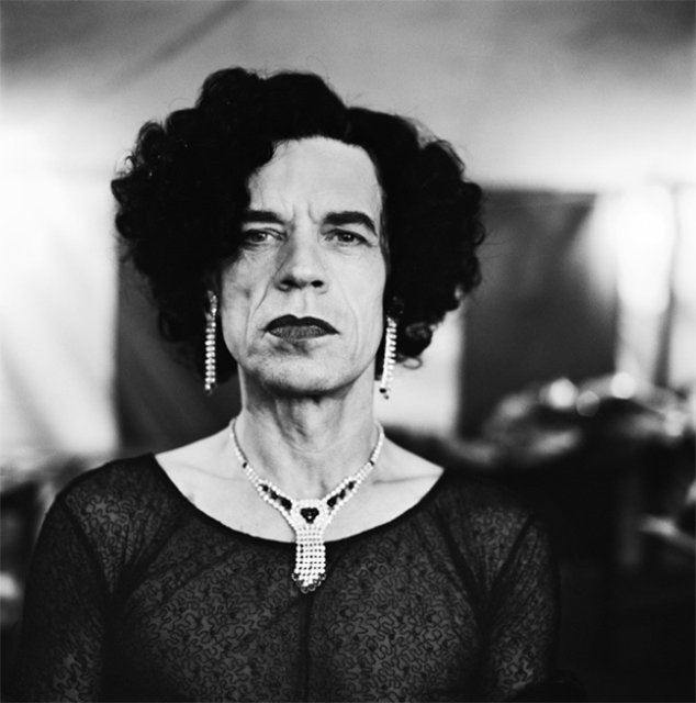 Anton Corbijn primo piano in bianco e nero di Mick Jagger con parrucca nera riccia orecchini pendenti trucco collana e maglia di pizzo trasparente nera