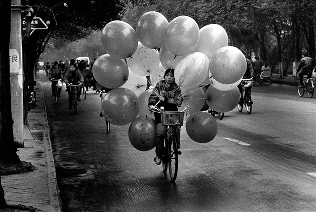 danilo de marco un tempo in cina foto in bianco e nero di ragazza cinese che va in bicicletta con in mano 20 enormi palloncini legati a fili