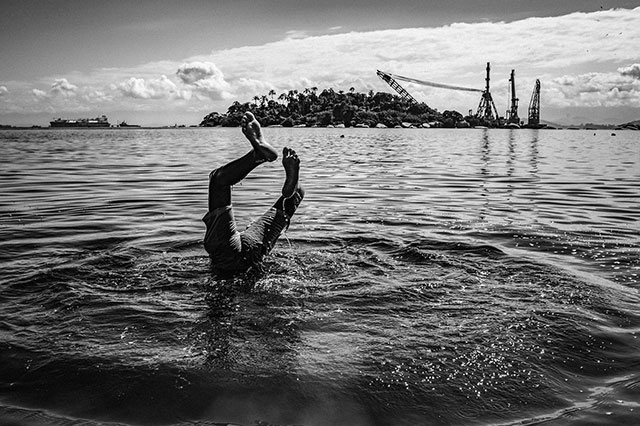 Molichrom 2022 Festival della fotografia nomade foto in bianco e nero con gambe di persona che escono dal mare sullo sfondo isoletta una nave e delle gru