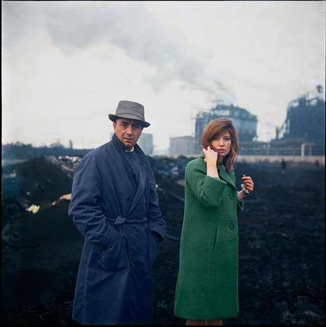 Enrico Appetito "Antonioni e Vitti: una storia d'amore e di cinema" il regista Antonioni con mani in tasca di cappotto blu e cappello grigio e l'attrice Monica Vitti con cappotto verde e mano sinistra che tocca i capelli guardano in camera con aria seria.alle spalle campo con terra nera e sullo sfondo palazzi in costruzione