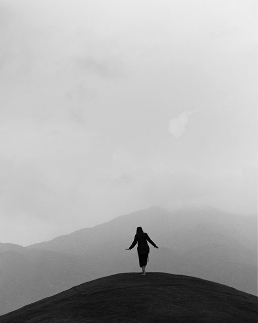 Clara Gassull e Israel Ariño foto in bianco e nero di donna in lontananza di spalle su cima di una collina davanti a paesaggio nebbioso di montagne