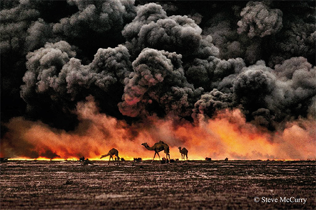 Steve McCurry Animals deserto con in lontananza gruppo di cammelli con alle spalle cielo completamente ricoperto da fumo nero e fuoco