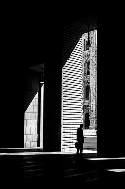 andrea rotili foto in bianco e nero di uomo in ombra sotto un portico che guarda verso il duomo di Milano di cui si scorge un dettaglio