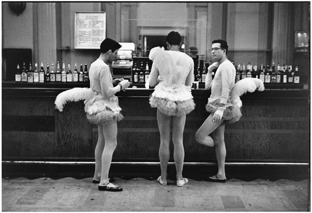 elliott erwitt foto in bianco e nero di tre uomini vestiti da ballerine con calze bianche tutu e coda di piuma al bancone di un bar