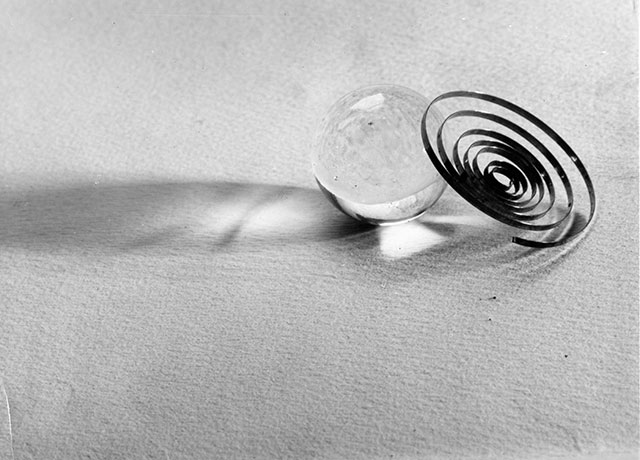 emanuele e giuseppe cavalli foto in bianco e nero con una biglia di vetro trasparente e una spirale che riflettono l'ombra su un piano