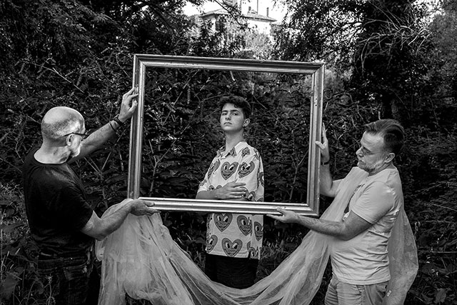 Gianni Rauso Roma foto in bianco e nero di due uomini che tengono una cornice vuota davanti ad un ragazzo in posa