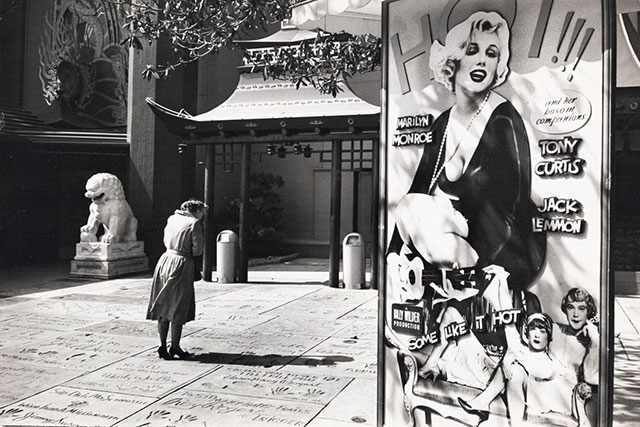 fotografe villorba foto in bianco e nero di donna per strada con mani sul viso vicino a cartellone di marilyn monroe