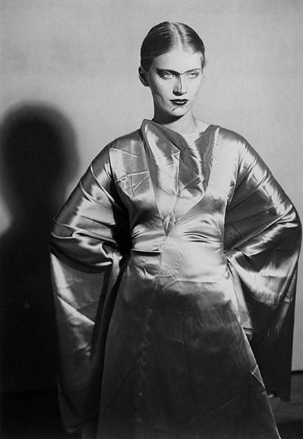 lee miller man ray foto in bianco e nero della fotografa e modella lee miller con capelli raccolti vestito chiaro di seta mani sui fianchi e segni di trucco sul naso mento e sopracciglia unite