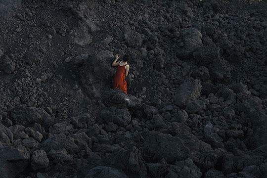 Simona Ghizzoni - Ferrara foto a colori di donna con vestito rosso che si arrampica su roccia nera