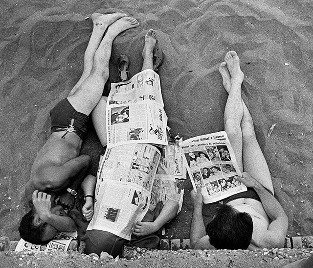 William Klein ROMA Plinio de Marchiis foto in bianco e nero vista dall'alto di tre persone stese sulla spiaggia appoggiate ad un muretto coperte da fogli di giornale