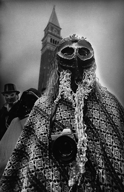 Graziano Arici Venezia foto in bianco e nero di persona con maschera di carnevale e macchina fotografica al collo durante il carnevale di Venezia
