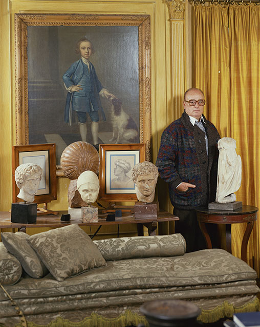 Mauro Bolognini Pistoia foto a colori di Mario Bolognini fotografato in un salotto con divano statue cornici e un grande quadro
