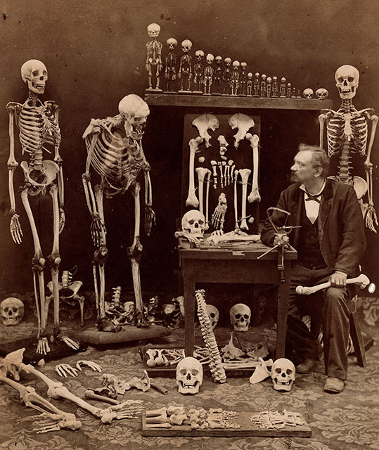 L'occhio della scienza Pisa foto seppiata di uomo seduto che guarda scheletri appesi nella stanza piena di teschi e ossa