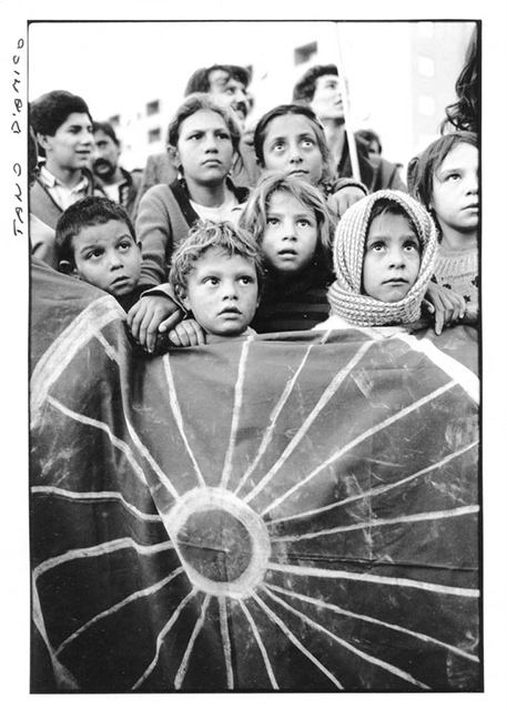 Tano D'amico Roma foto in bianco e nero di gruppo di bambini che guardano in alto appoggiati ad un telo con disegnata una ruota