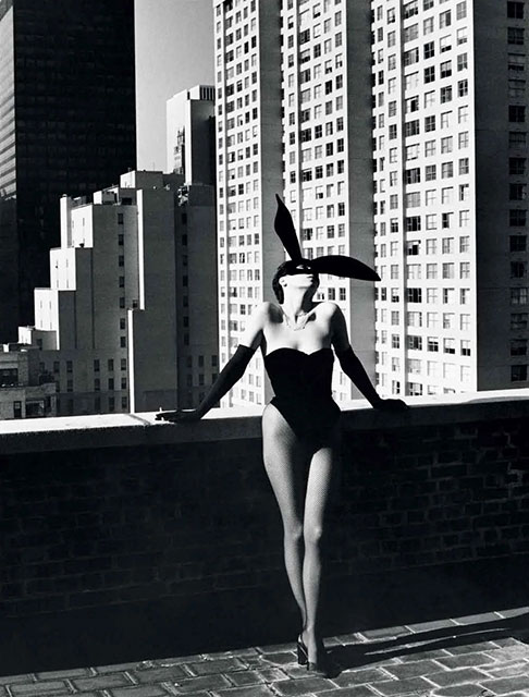 Helmut Newton Milano foto in bianco e nero di modella vestita da coniglietta appoggiata a muro su terrazzo con alle spalle grattacieli