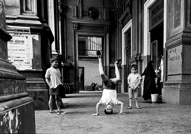 Gianni Berengo Gardin Napoli foto in bianco e nero di due bambini che guardano un terzo bambino che fa una capriola sotto un portico