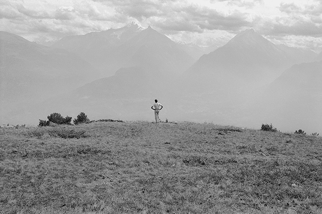 Mario Cresci Aosta foto in bianco e nero di uomo di spalle in lontananza in un prato che guarda le montagne