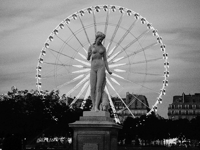 Stand E 015 Milano foto in bianco e nero di statua di donna con cane con dietro ruota illuminata del luna park