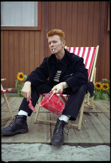 Marck Allan Bologna foto a colori del cantante David Bowie seduto su sdraio a righe bianche e rosse con sigaretta in bocca e secchiello e paletta rossi in mano